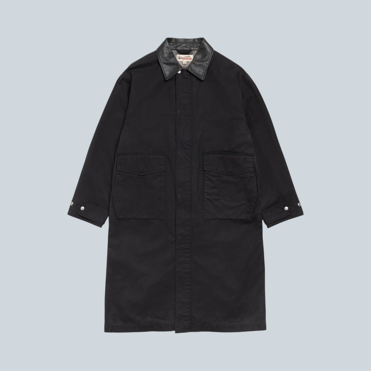 Manteau duster Stüssy noir en coton avec col contrastant et grandes poches avant, disponible chez Saison