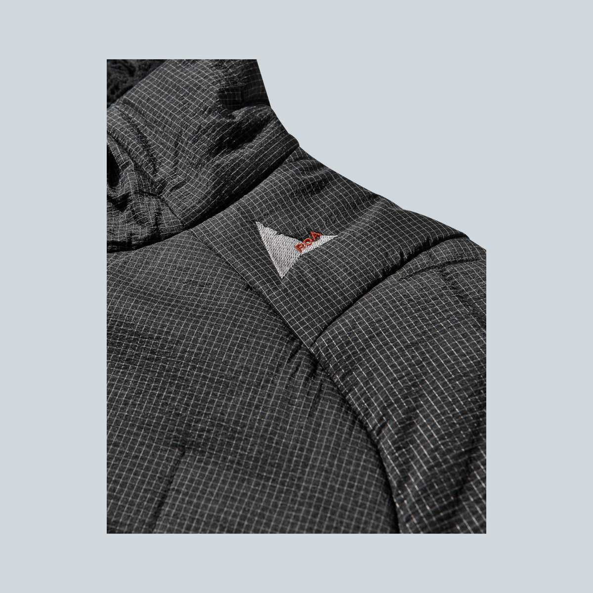 Gros plan sur la veste isolante noire Saison Merapi Ethermaloft avec texture quadrillée et logo brodé